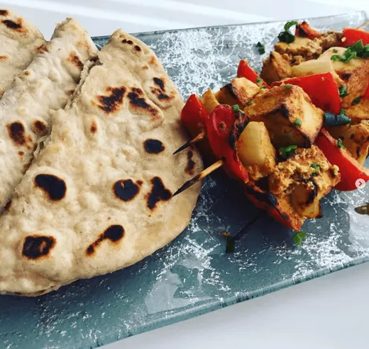 Paneer tikka and pepper skewers beside charred naan