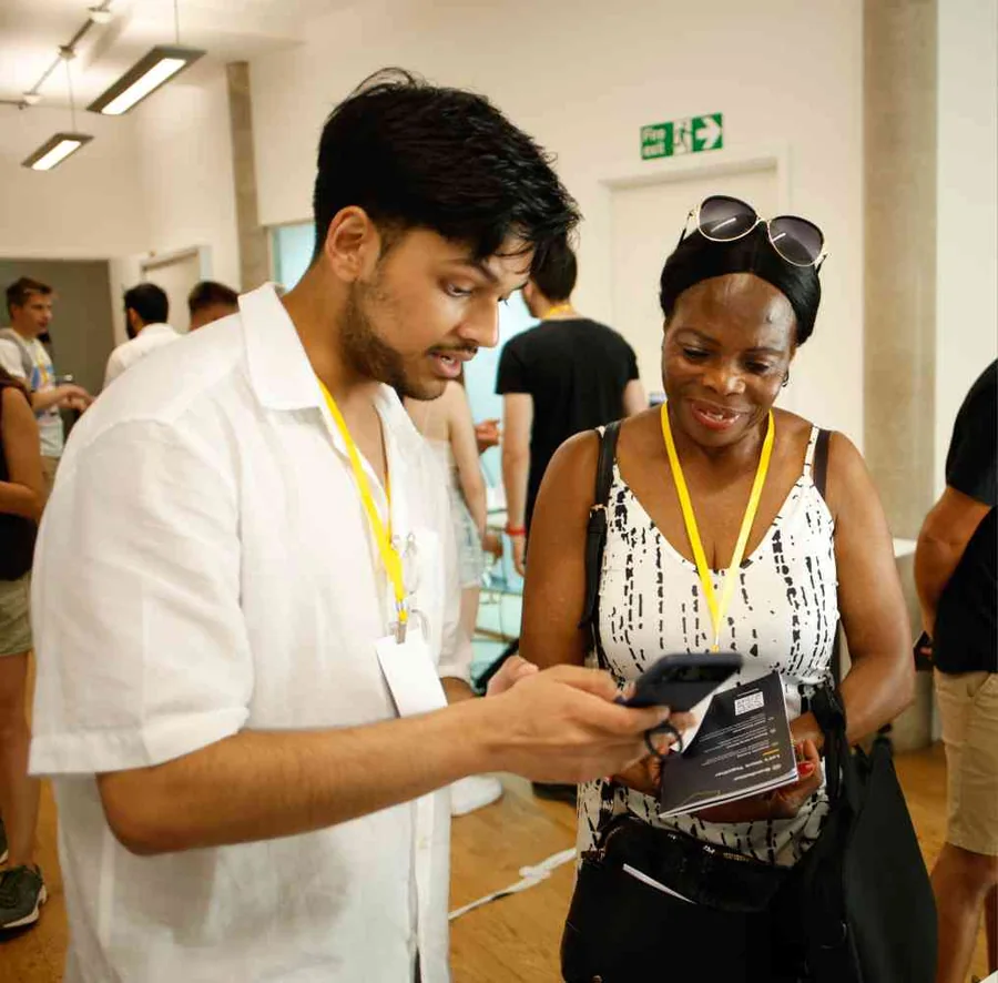Mahin showing his project on his phone to a visitor at the UX bootcamp’s Demo Day, both wearing yellow lanyards